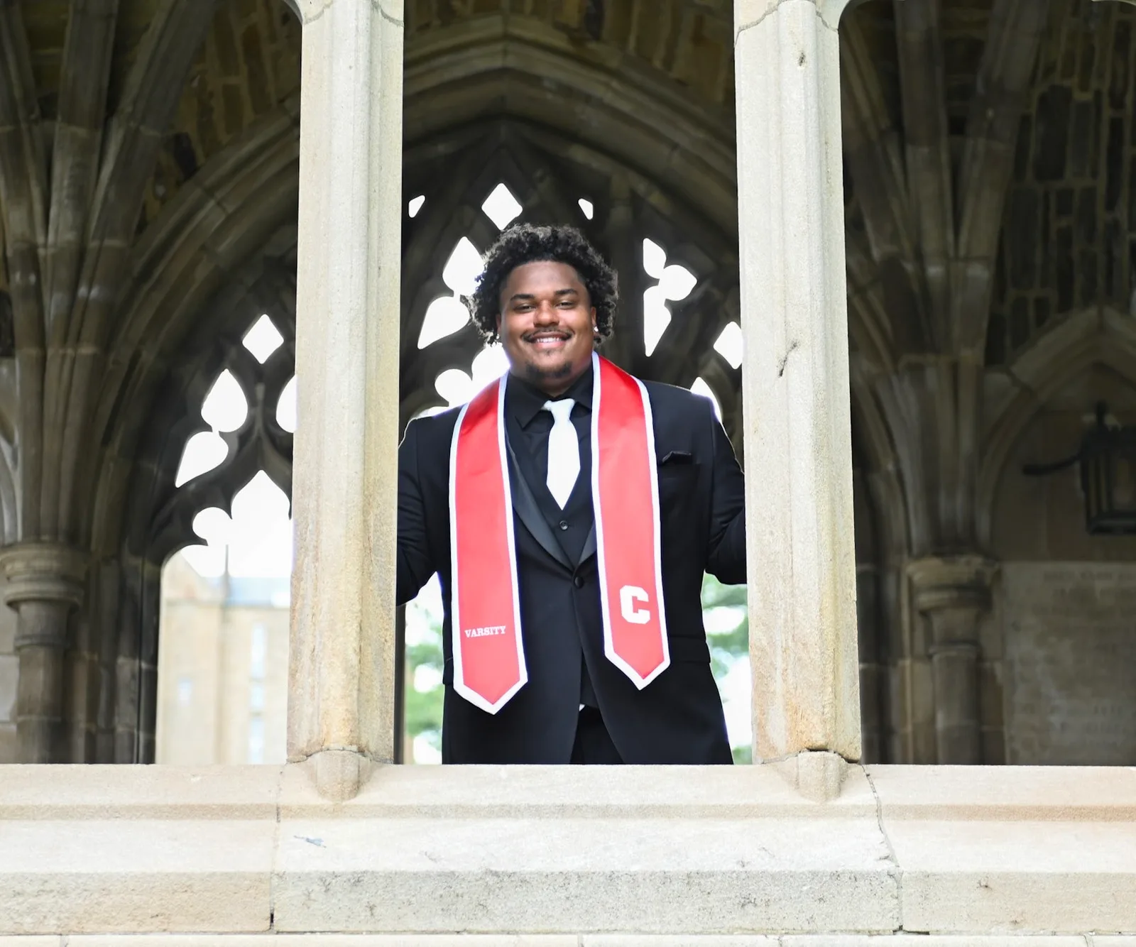 Terrance Caldwell at Cornell University in a black suit and a red Cornell Varsity stole, smiling between stone Gothic arches